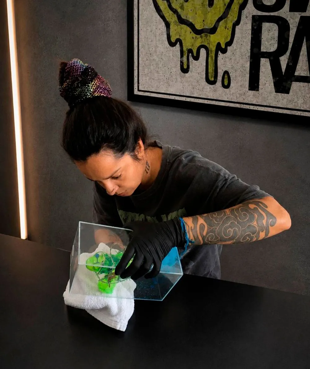 Dani Coelho finalizando a obra Contenção, uma caixa acrílica com arma de brinquedo e arame farpado